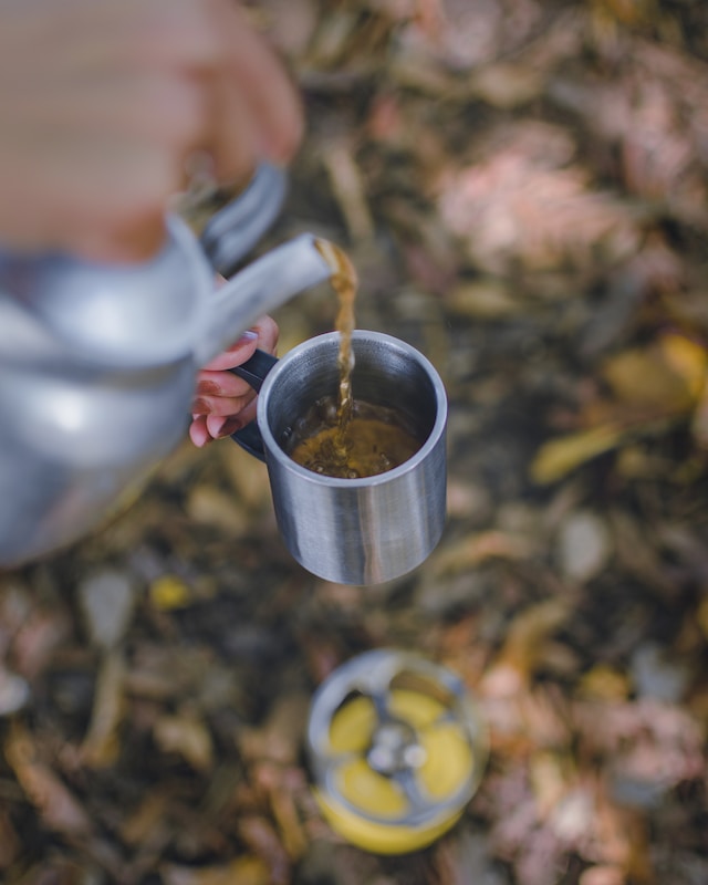 Photo of tea being pour from a kettle above a camping stove.